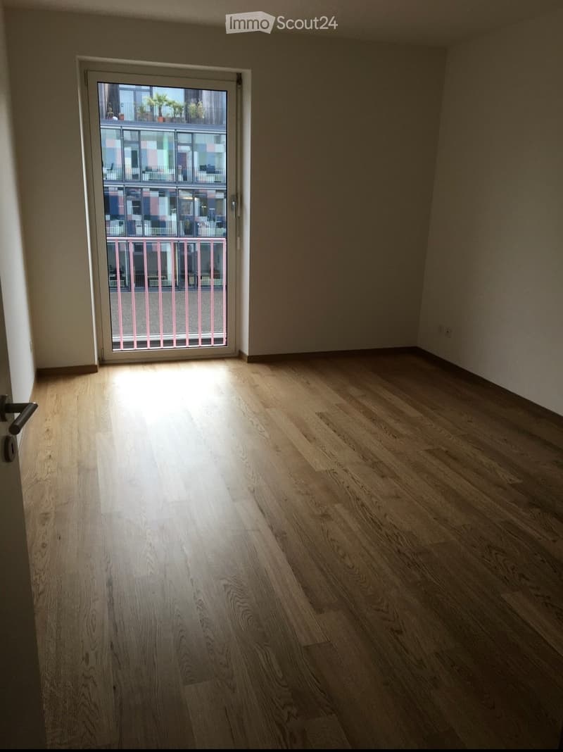 Empty room with light wooden flooring and a sliding glass door leading to a balcony.