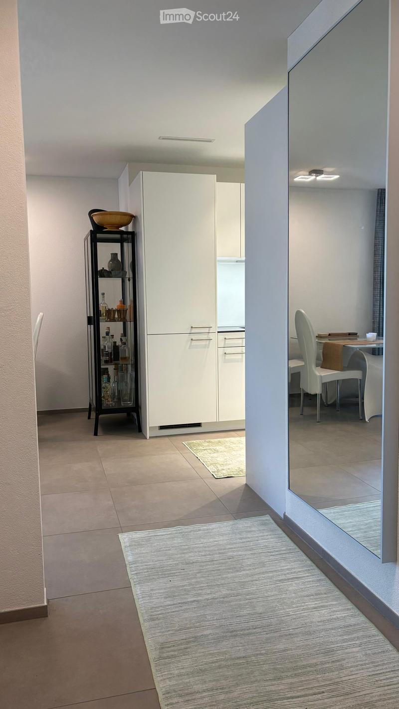 Modern, minimalist room with a white cabinet, a glass shelf with decorative items, a small table with chairs, and two rugs on the floor.