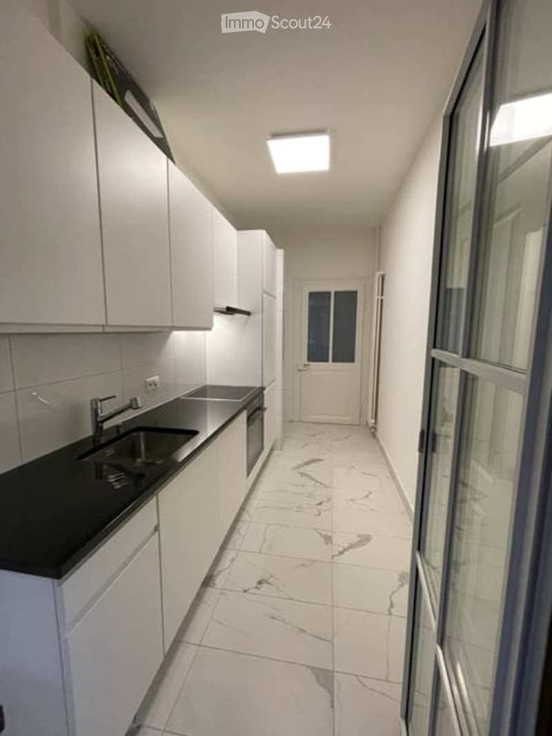 Modern kitchen with white cabinets, black countertop, stainless steel sink, and marble flooring.