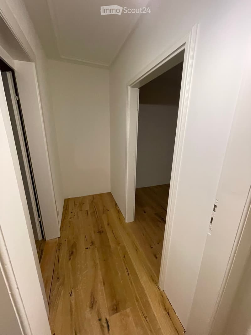 Empty hallway with light wooden flooring and white walls, featuring two open doorways leading to adjacent rooms.