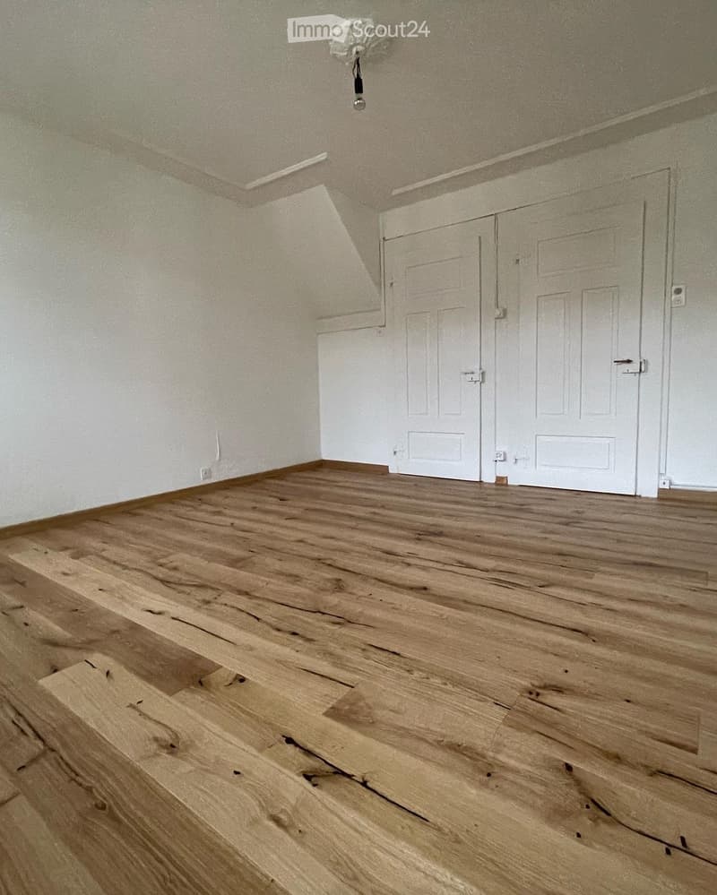 Empty room with wooden flooring and white walls, featuring two white doors and a visible electrical outlet.