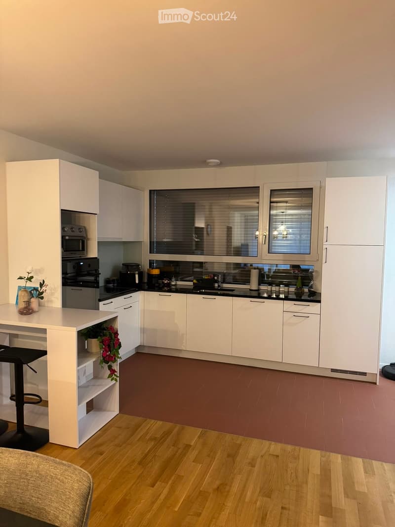 Modern kitchen with white cabinets, stainless steel appliances, island with bar stool, and decorative items on the counter.