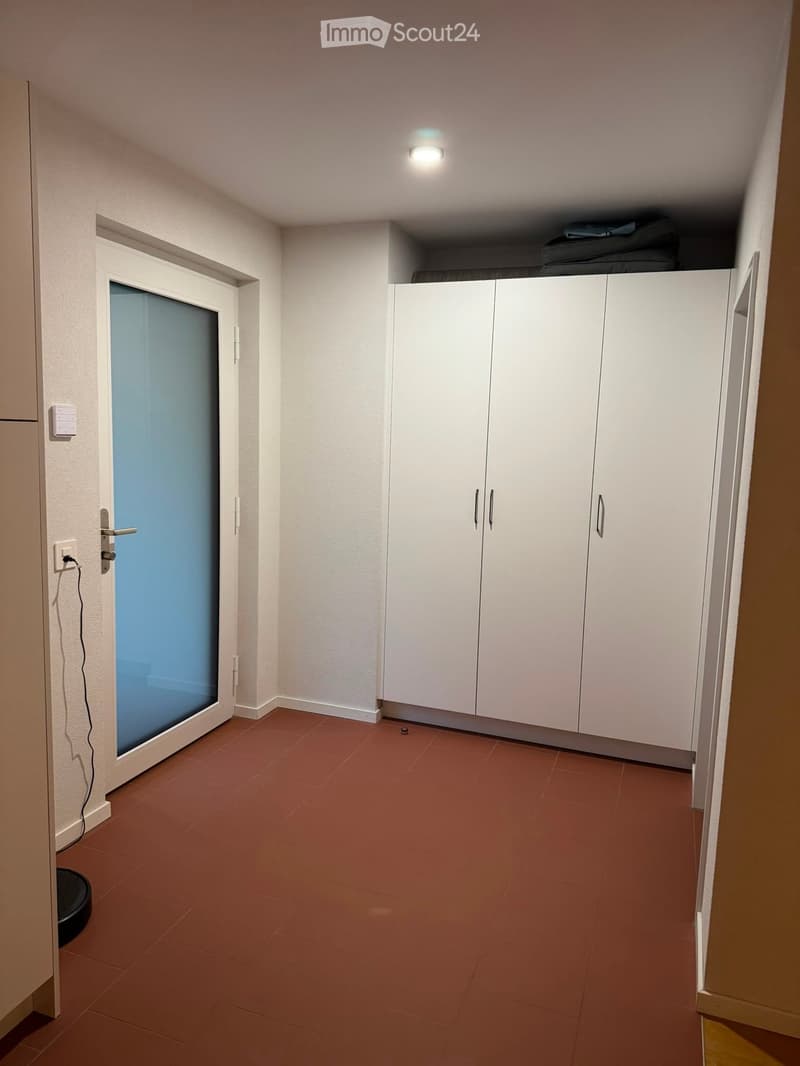 Empty hallway with white walls, red tiled floor, white cabinetry, and a frosted glass door.
