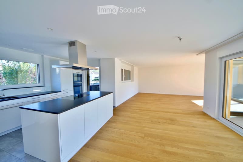 Modern kitchen with white cabinets, black countertops, a central island, and built-in appliances including a sink, oven, and range hood. The space features light wooden flooring and large windows allowing natural light.