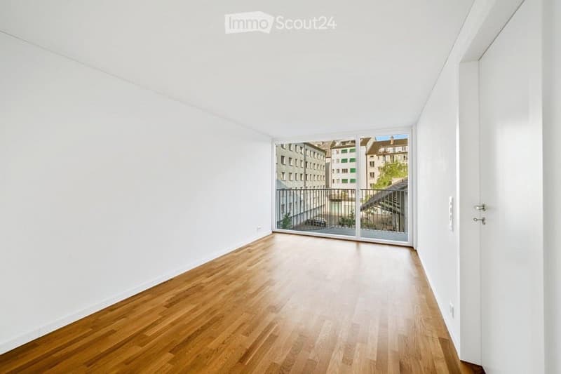 Empty room with wooden flooring, white walls, and a large sliding glass door leading to a balcony.