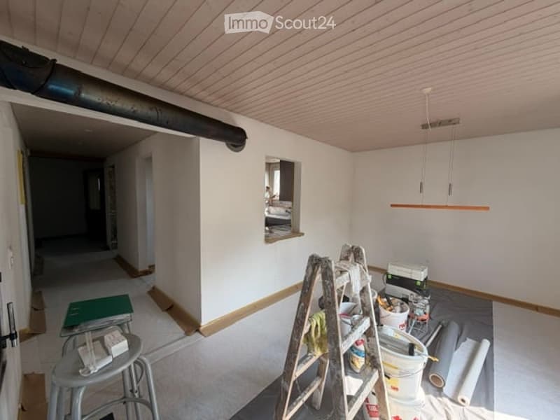 Empty room with white walls, wooden floor, and a ladder with construction materials. No furniture or equipment.