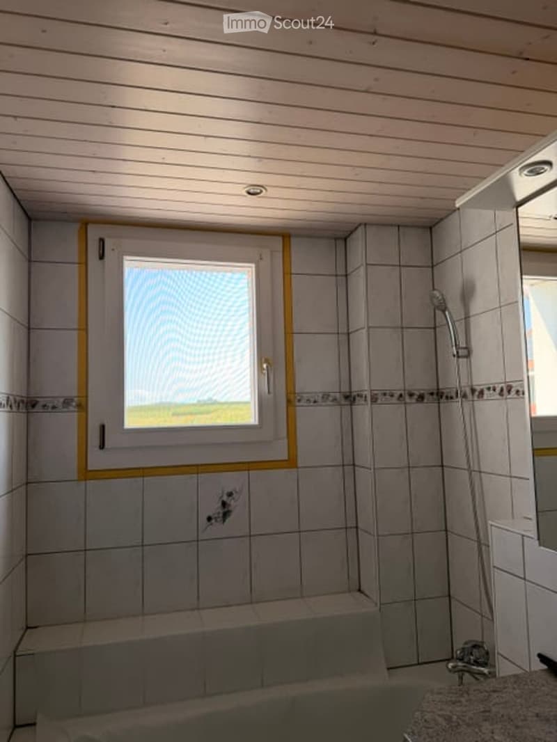 Modern bathroom with white tiled walls, a bathtub, a shower, and a window with blinds.