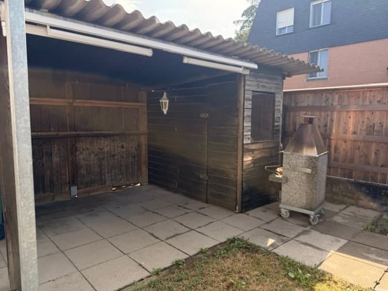 Outdoor patio with tiled floor, wooden garage, and a grill on wheels.
