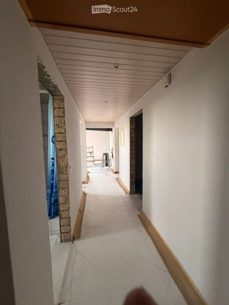 Clean, modern hallway with white walls, light wooden ceiling, and tiled floor. Doors on both sides lead to various rooms.