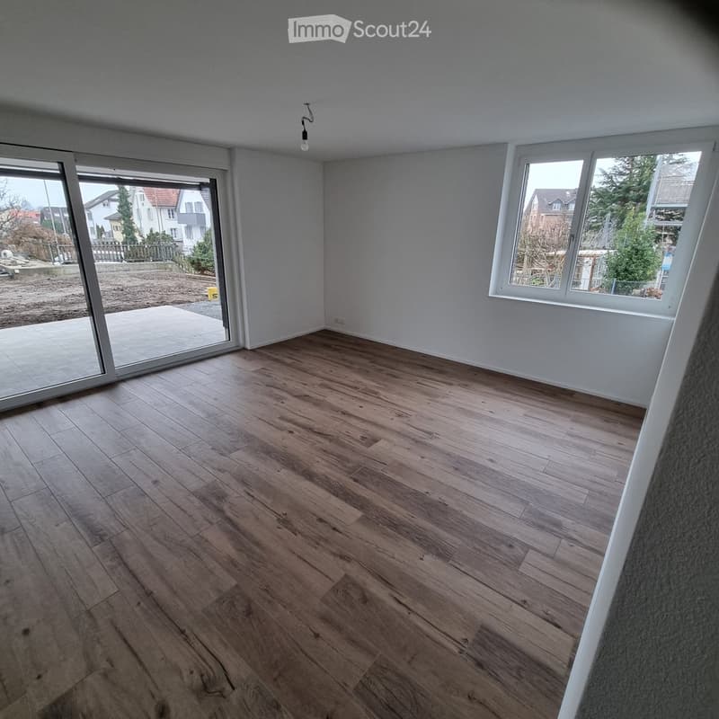 Empty room with wooden flooring, large windows, and a sliding glass door leading to a patio.