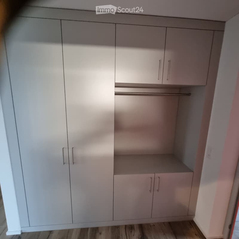 Empty closet with white built-in cabinets and a wooden floor. No furniture or items present.