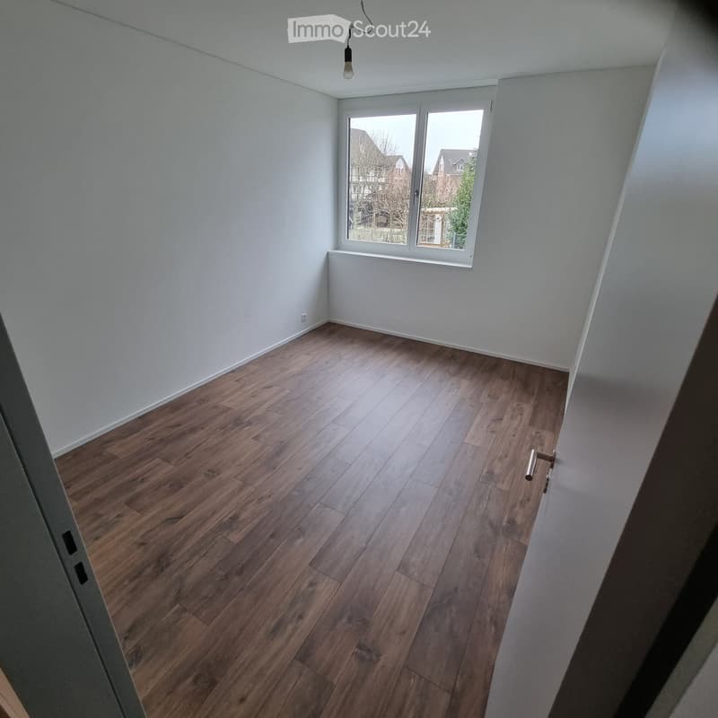 Empty room with wooden flooring, white walls, and a large window with white frame. No furniture or equipment present.