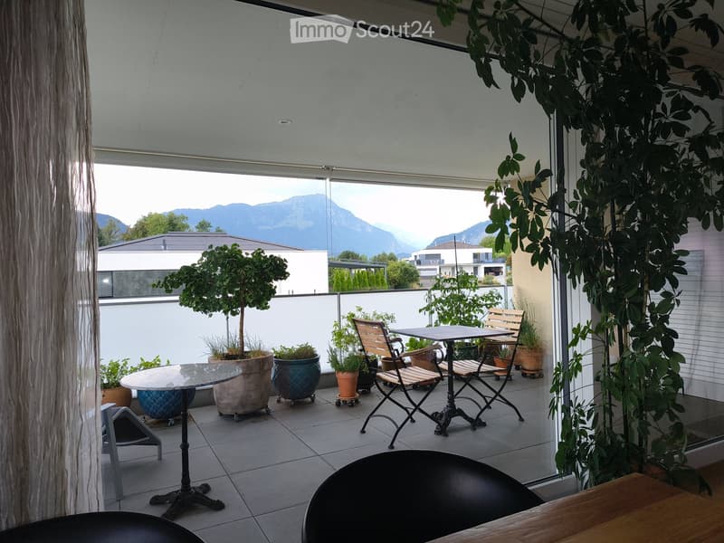 Balcony with a view of mountains, featuring a table, chairs, and potted plants.