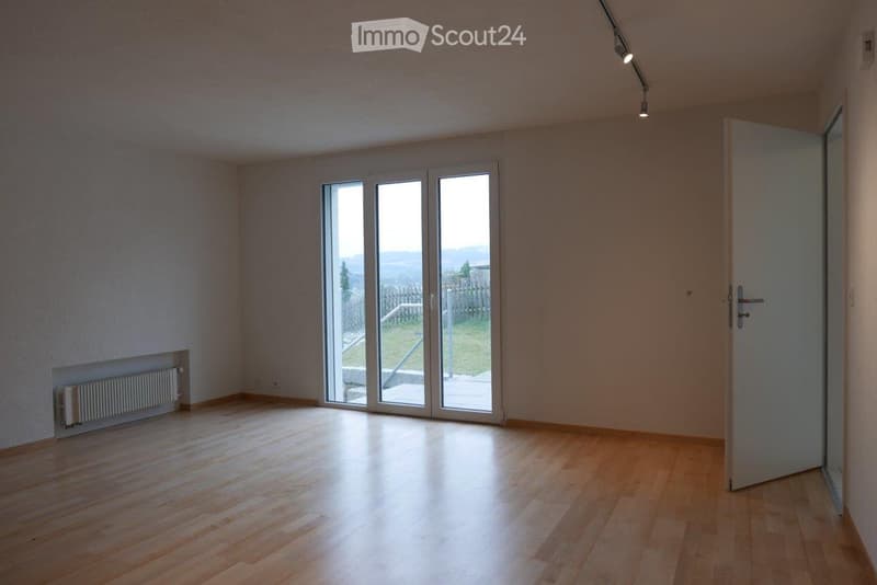 Empty room with wooden flooring, large sliding glass doors leading to a patio, and a radiator on the left wall.
