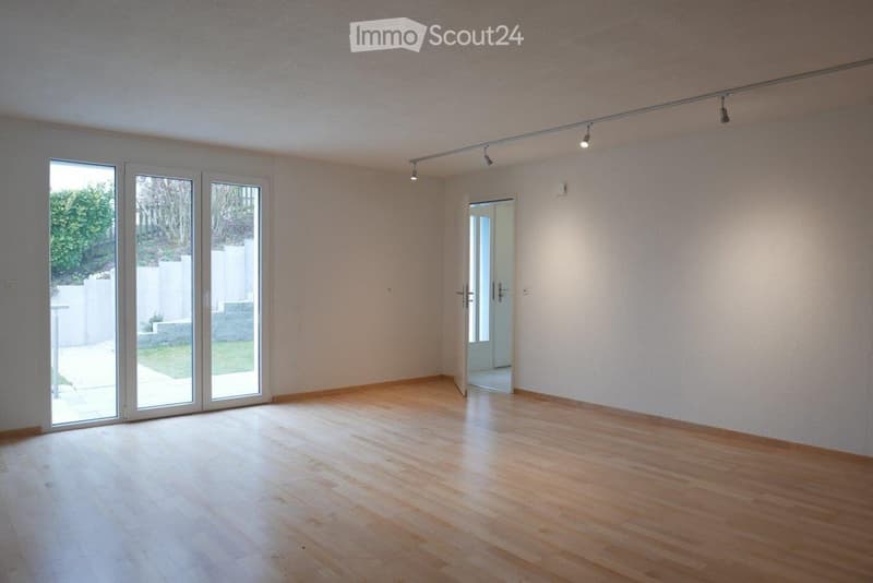 Empty room with light wooden flooring, white walls, large glass sliding doors leading to an outdoor area, and recessed lighting.