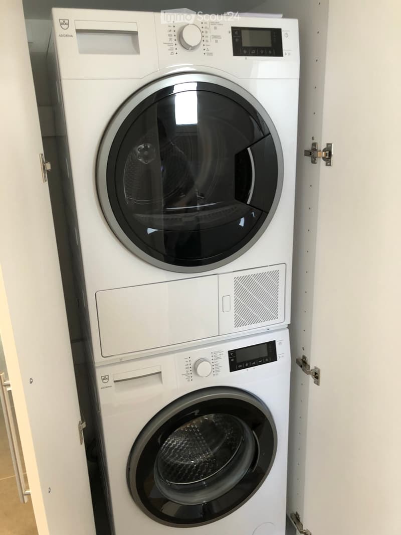 A compact, stacked washing machine and dryer unit in a white bathroom setting.