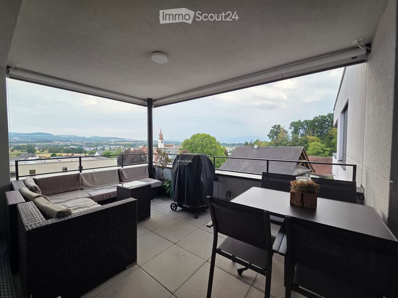 Balcony with a view, featuring a wicker sofa, a dining table with chairs, and a covered grill.