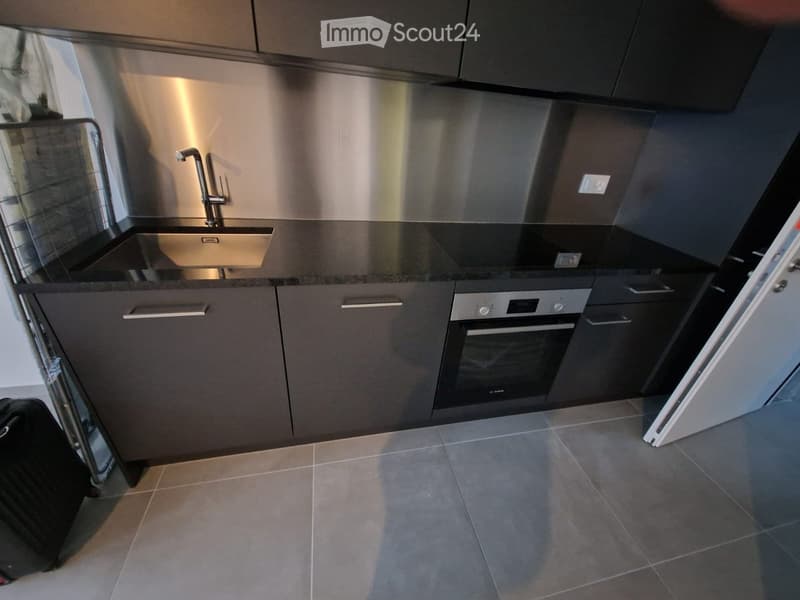 Modern kitchen with stainless steel sink, faucet, built-in oven, and dark grey cabinets.
