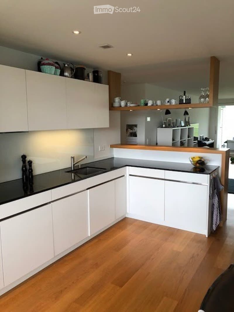 Modern kitchen with white cabinets, black countertops, and a wooden floor. Features a sink, faucet, and various decorative items on the counter and shelves.