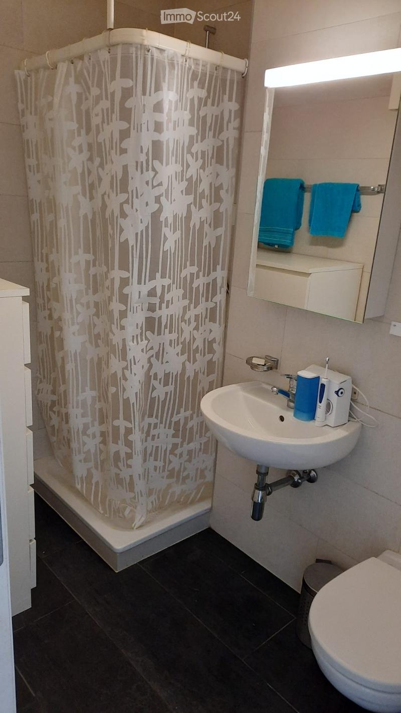 Modern bathroom with dark tiled floor, white sink, mirror, and shower with decorative curtain. Blue towels are neatly placed on the shelf above the sink.