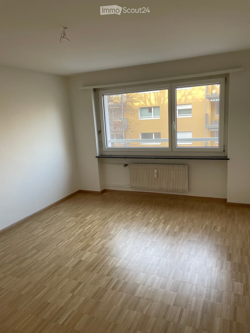 Empty room with wooden flooring, white walls, and a large window with a radiator below it.