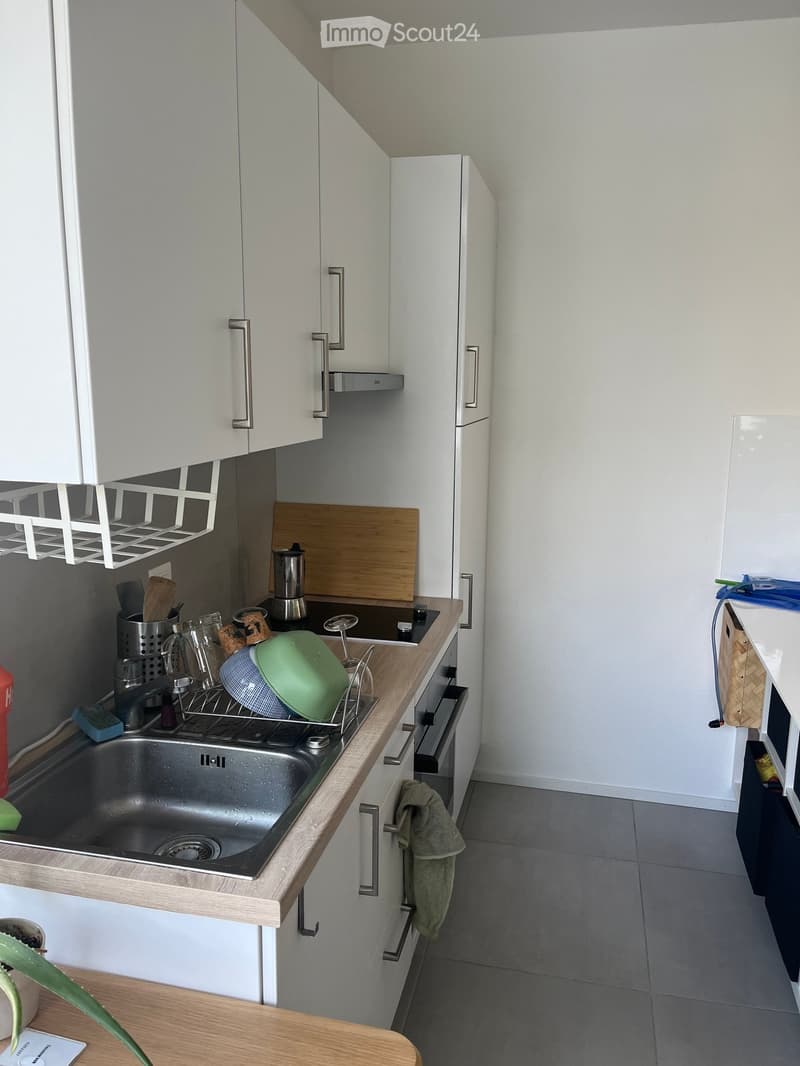 Modern kitchen with white cabinets, stainless steel sink, wooden countertop, and various kitchen items including a cutting board, frying pan, and dish rack.