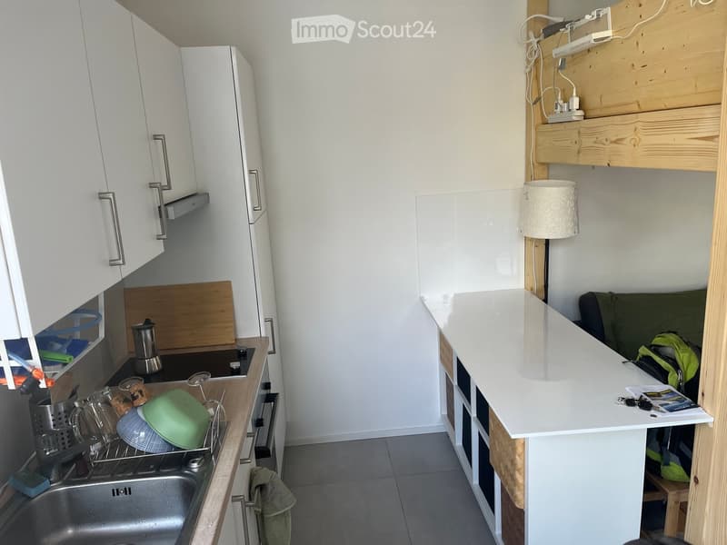 Compact kitchen area with white cabinets, a sink, dish rack, and a small living space with a sofa and lamp.