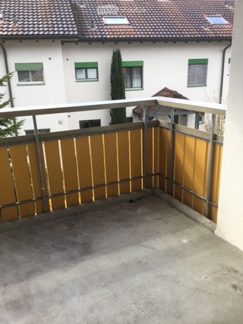 Balcony with wooden paneling and metal railing, overlooking a residential area with houses and trees.