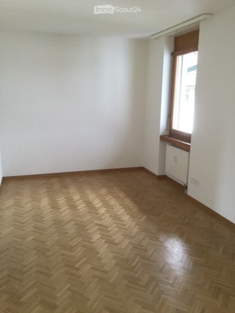 Empty room with wooden herringbone flooring, white walls, and a single window with a small wooden sill.