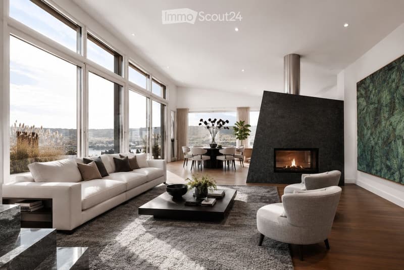 Modern living room with large windows offering a scenic view, a white sectional sofa, a black coffee table, a fireplace, and a dining area with a round table and chairs.