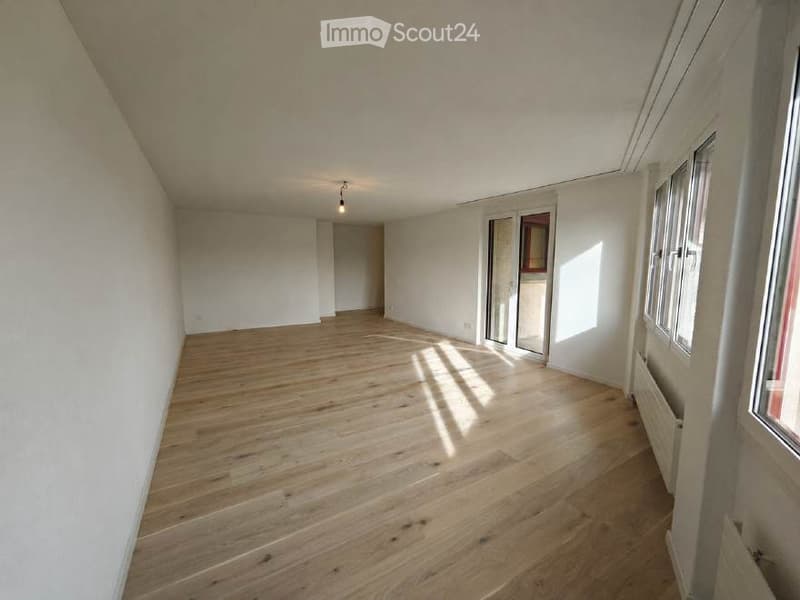 Empty room with wooden flooring, white walls, and large windows allowing natural light to enter. No furniture or equipment is present.