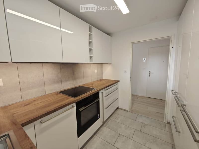 Modern kitchen with white cabinets, wooden countertop, built-in oven, and white tiled floor.