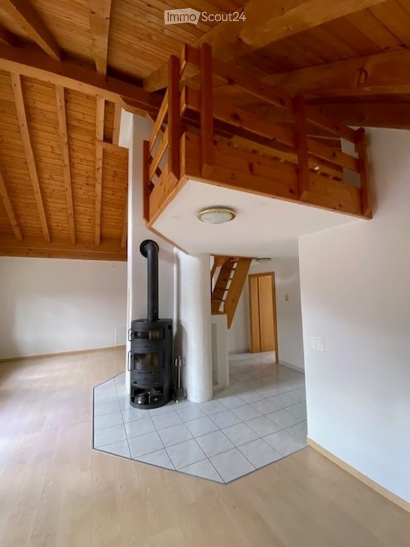 Bright hallway with wooden floors, white walls, and a visible staircase leading to an upper level. A wood-burning stove is placed near the wall.