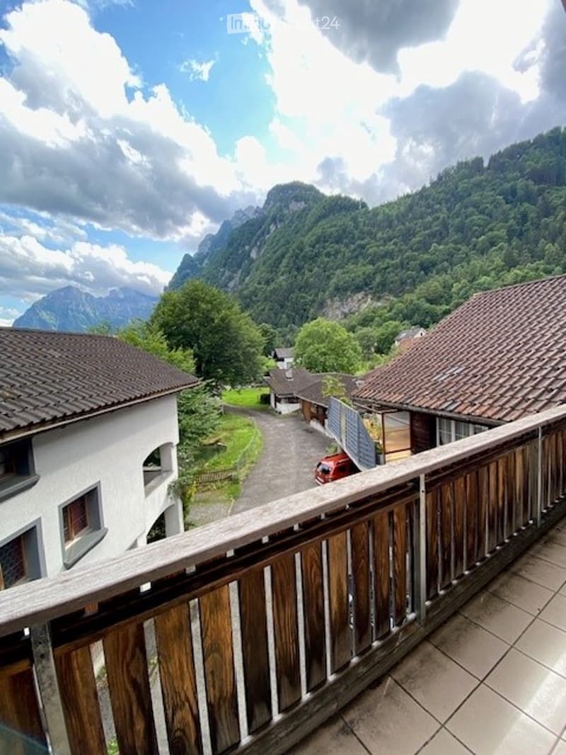 Balcony overlooking a scenic valley with houses, trees, and mountains in the background.
