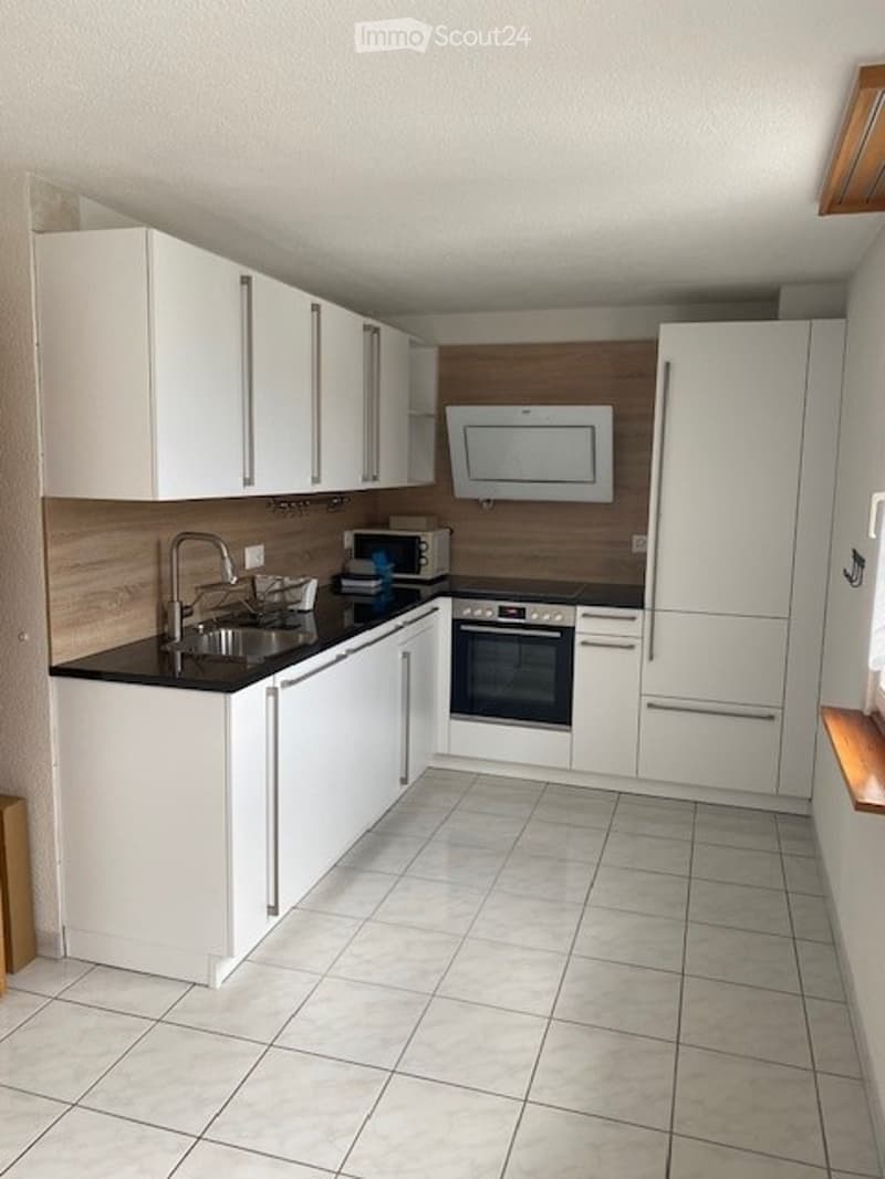 Modern kitchen with white cabinets, black countertops, and stainless steel appliances including a sink, microwave, oven, and refrigerator.
