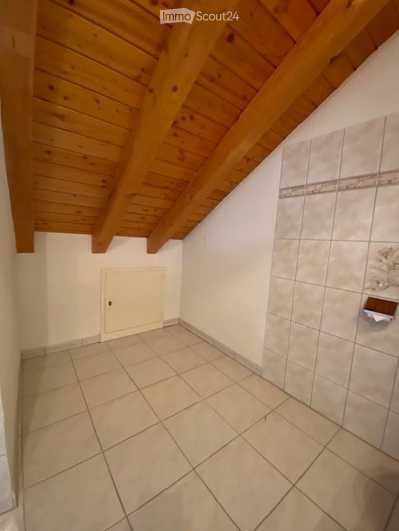 Empty bathroom with tiled floor and walls, wooden slanted ceiling, and a closed white door.