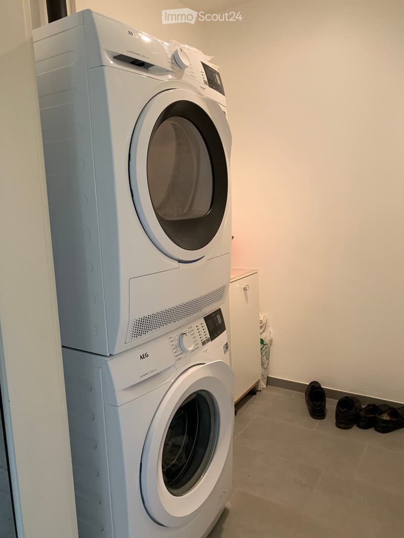 A small bathroom with a stacked washing machine and dryer unit, light-colored walls, and tiled floor.