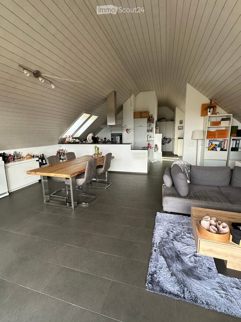Modern living and dining area with grey sofa, coffee table, dining table with chairs, kitchen island, and bookshelf.