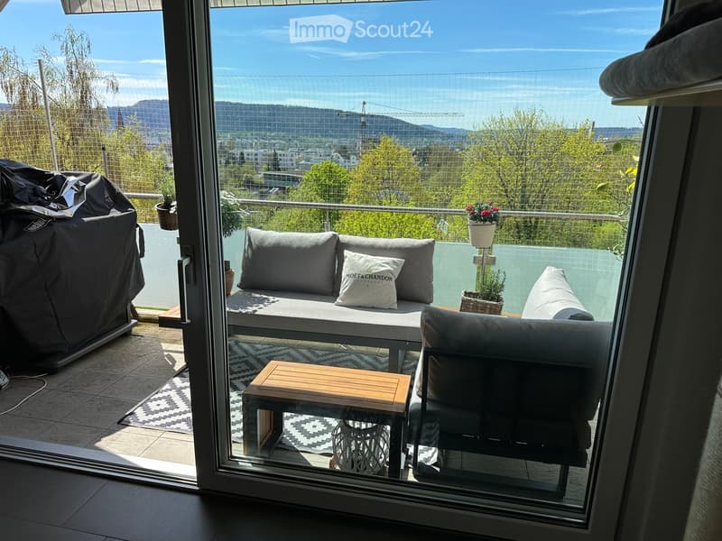 Balcony with a sofa, chair, small table, and potted plants, offering a scenic city view.