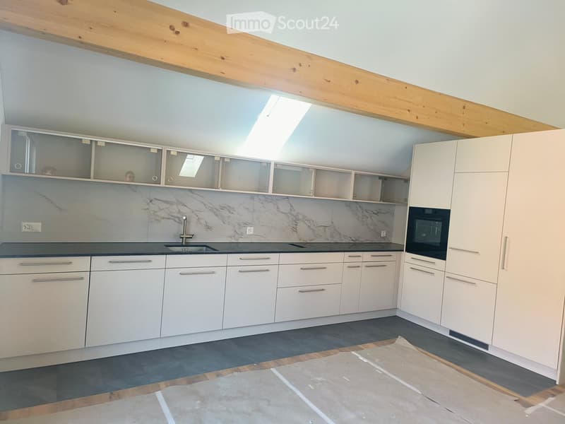 Modern kitchen with white cabinets, marble backsplash, and stainless steel sink and oven. Exposed wooden beams on the ceiling and a skylight provide natural light.
