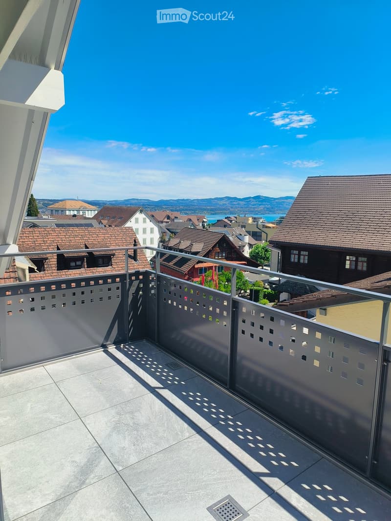 Balcony with modern metal railing, tiled floor, and scenic view of a town with houses and mountains in the background.