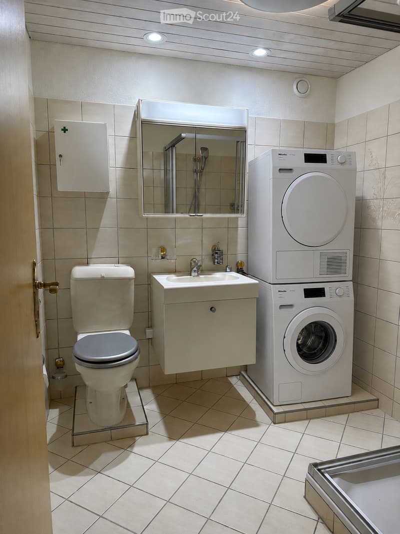 Modern bathroom with beige tiles, a toilet, a sink with a cabinet, a mirror, and a stacked washer/dryer unit.