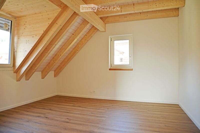 Empty attic room with wooden beams, wooden floor, and two windows.