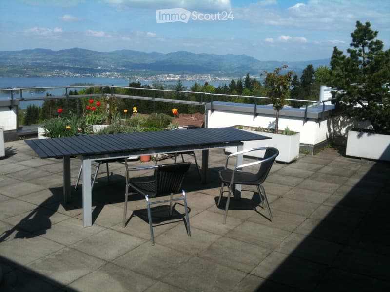 Balcony with a table and two chairs, overlooking a scenic lake and mountain view.