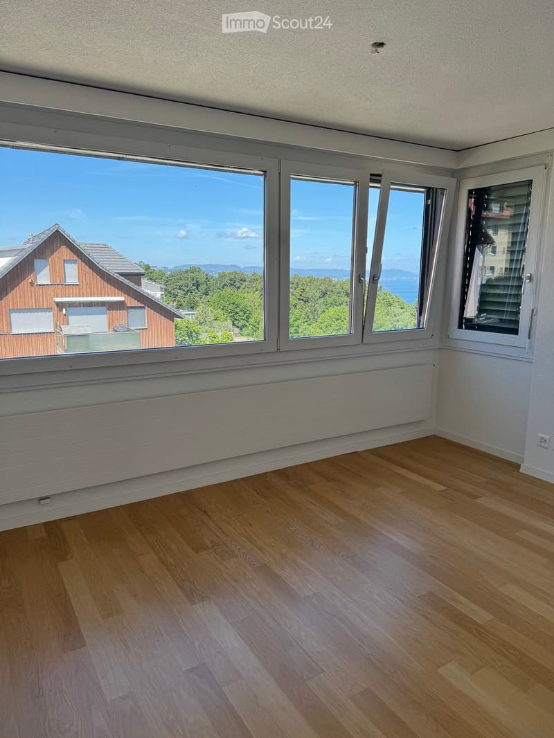 Empty room with wooden flooring, large windows offering a scenic view, and white walls.