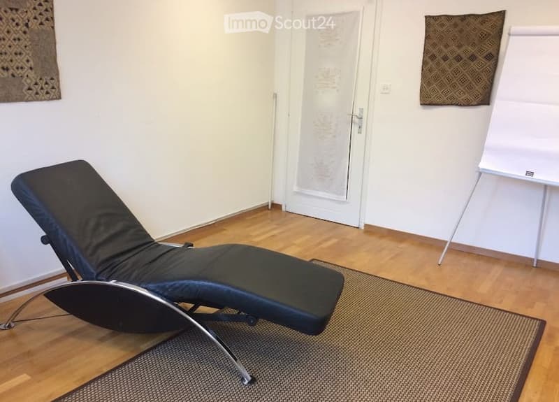 A modern, minimalist room with a black leather lounge chair, a white screen, and two patterned tapestries on the walls.