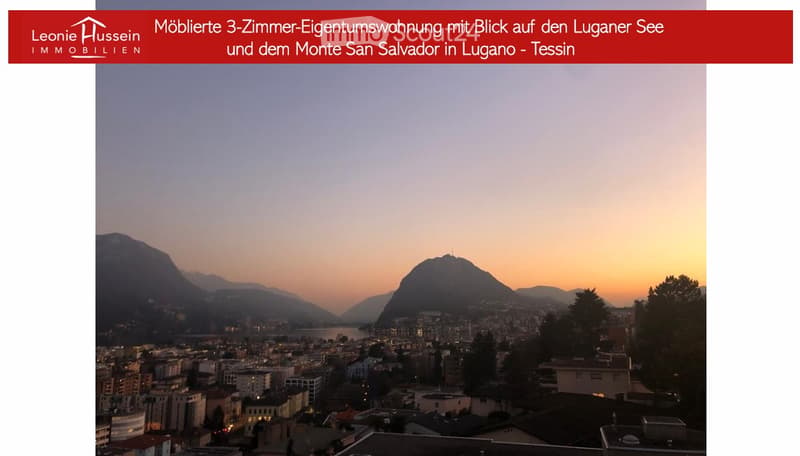Panoramic view of Lugano Lake and Monte San Salvador at sunset, with cityscape and surrounding mountains visible.