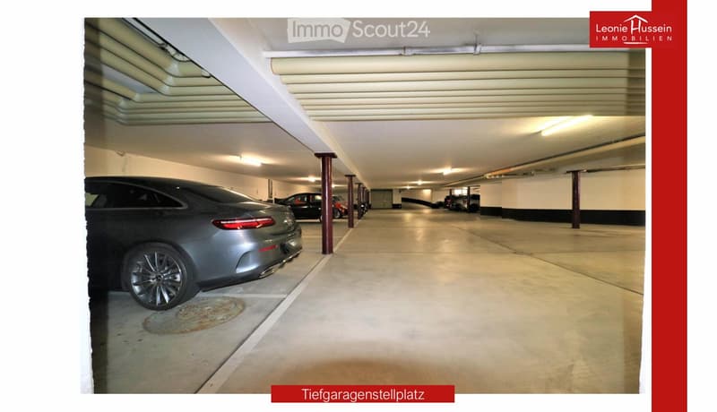 Underground parking area with several parked cars, concrete floor, white ceiling, and red support pillars.