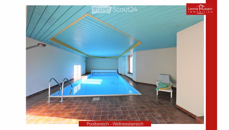 Indoor swimming pool area with tiled floor, metal handrails, lounge chair, and bright blue ceiling.