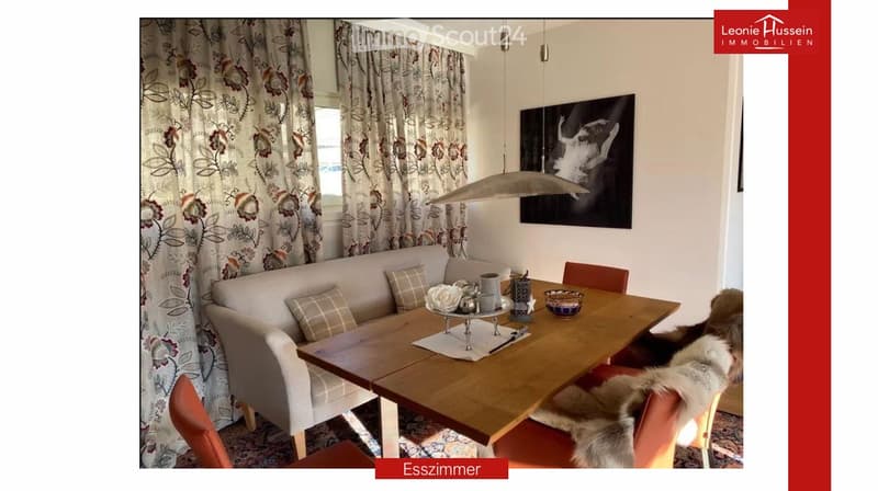A cozy dining and living area with a sofa, a wooden dining table, chairs, a pendant light, and a picture frame on the wall.